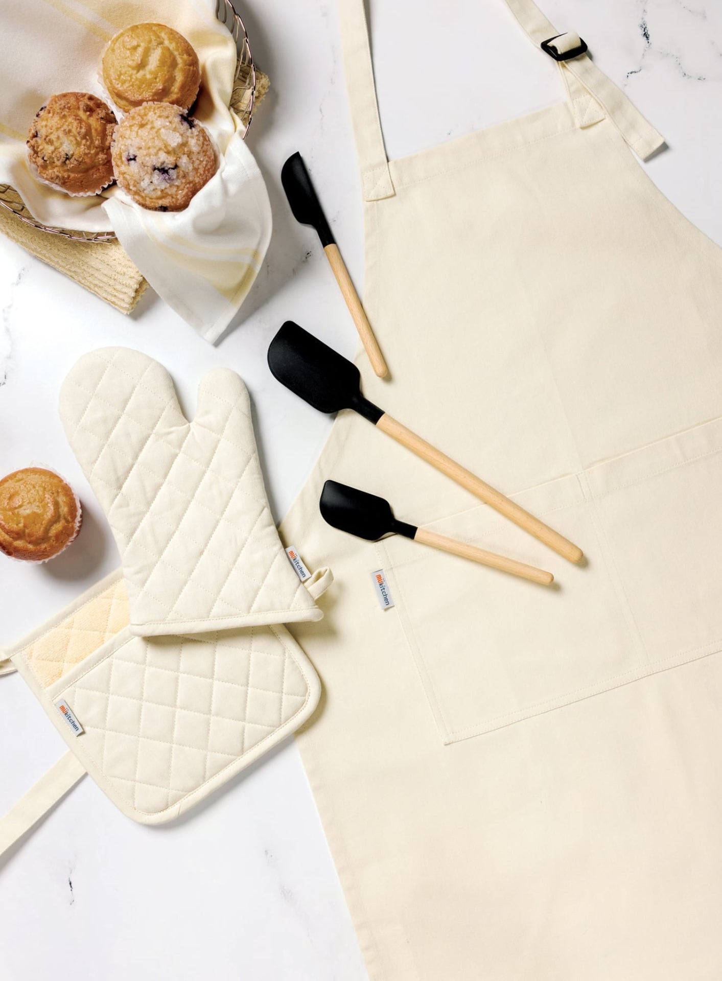 Baking tools and apron on a white surface with muffins.