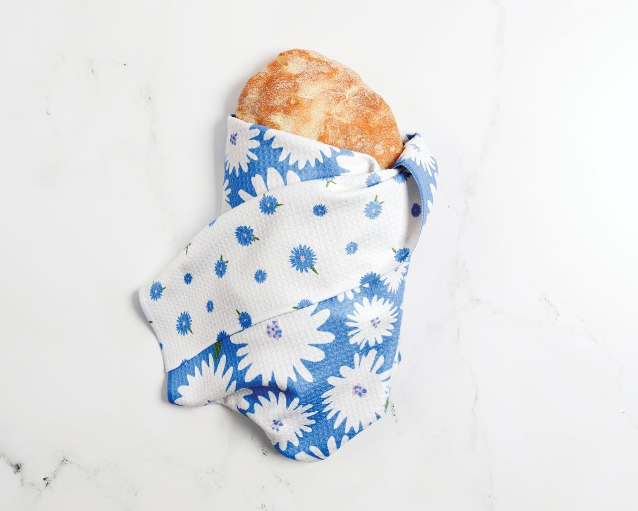 Bread wrapped in a blue and white floral cloth on a light gray surface